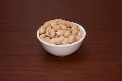 Peanuts uncleaned against a background of brown wood. Stock Photos