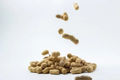 Peanuts on a white background. A peanut falls on a pile of peanuts.  Stock Photos