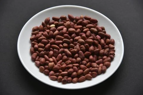 Peanuts on a white plate on a black background. Delicious nutty breakfast. Stock Photos