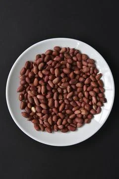 Peanuts on a white plate on a black background. Delicious nutty breakfast. Stock Photos