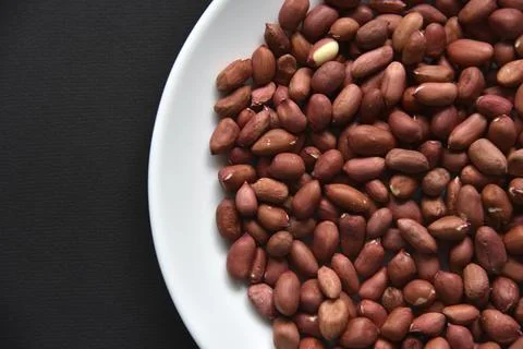 Peanuts on a white plate on a black background. Delicious nutty breakfast. Stock Photos