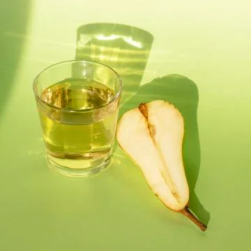 Pear split in half and pear lemonade on green background with shadows from su Stock Photos
