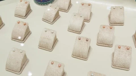 Pearl stud earrings organized on beige display stands, showcasing a collection Stock Footage 337470547