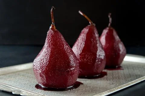 Pears in wine. Row of raditional dessert pears stewed in red wine on black ba Stock Photos
