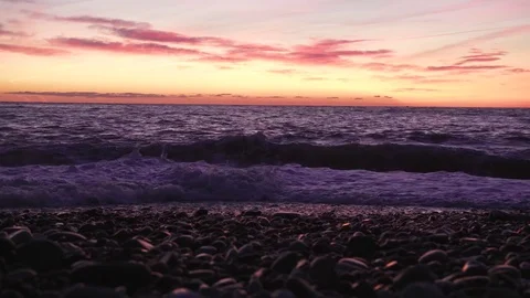 Pebble beach and surf in a duask at dramatic sunset over waving sea Stock Footage 79091025