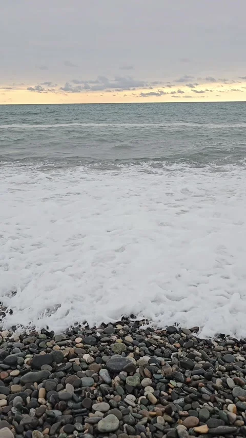 Pebble beach with foamy sea waves and overcast sky during sunset Stock Footage 297615596