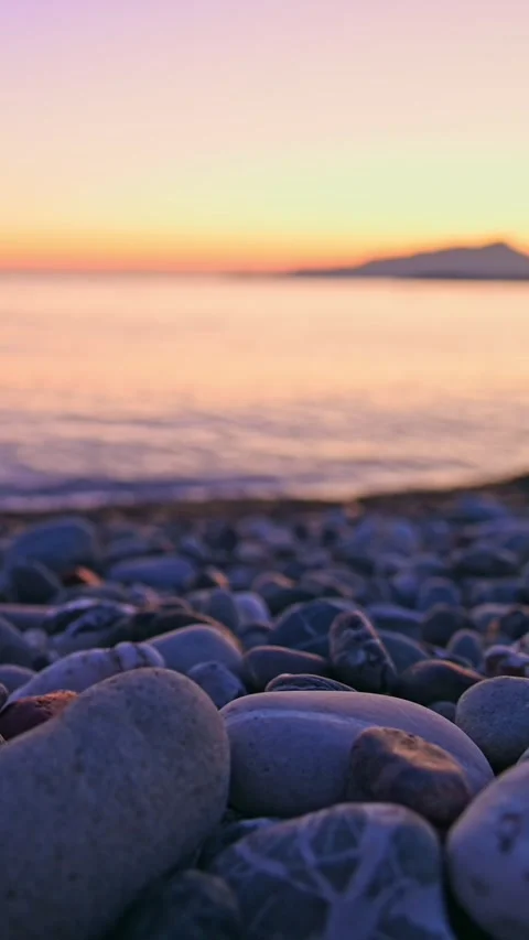 Pebble beach with gentle waves rolling toward shore at sunset Stock Footage 345080429