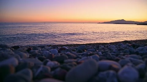 Pebble beach with gentle waves rolling toward shore at sunset Stock Footage 345080563