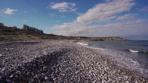 Pebble beach with gentle waves under blue sky, coastal apartments overlook Stock Footage 268621161