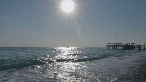 Pebble beach at sunset with floating people in the sea with big waves near the Видео 80104922
