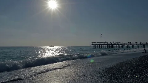 Pebble beach at sunset with floating people in the sea with big waves near the Stock Footage 80105223