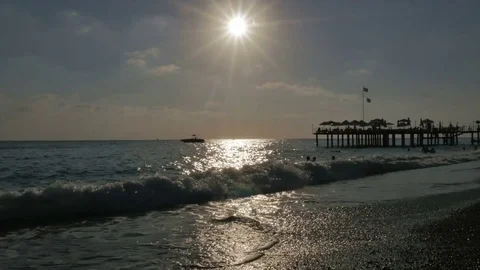 Pebble beach at sunset with floating people in the sea with big waves near the Stock Footage 80107128