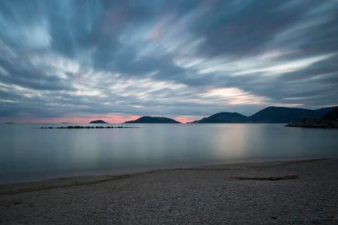 Pebble beach at sunset with moving clouds and silky sea Stock Photos