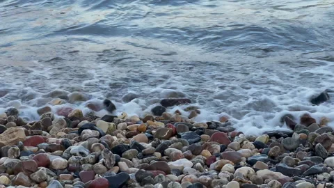 Pebble beach. Waves, surf. Stony coastline. Water of sea, ocean, river or lake. 動画素材 168703530