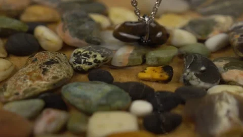 Pebble pendant with hole on silver chain swings over water  Stock Footage 258301788