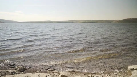 Pebble stone on coast with lake or sea water. Small waves slow motion Stock Footage 221017497
