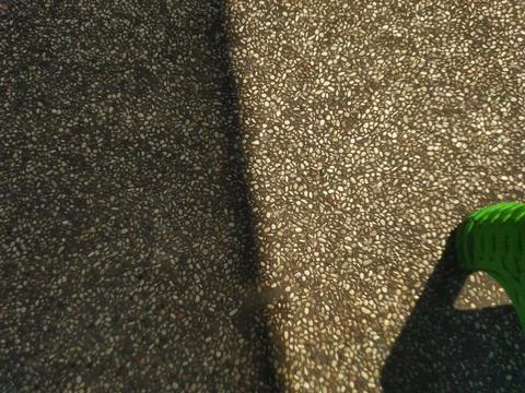 Pebbled concrete surface with strong diagonal shadow and bright green object Stock Photos
