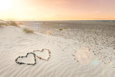 Pebbles arranged in shape of two hearts on sand beach ripples with beautiful Stock Photos