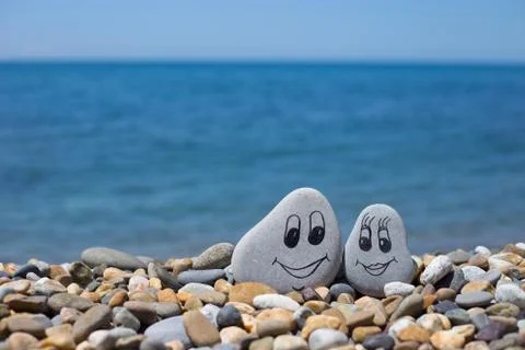 Pebbles with drawn faces in the sand. Loving couple. Travel concept. Stock Photos