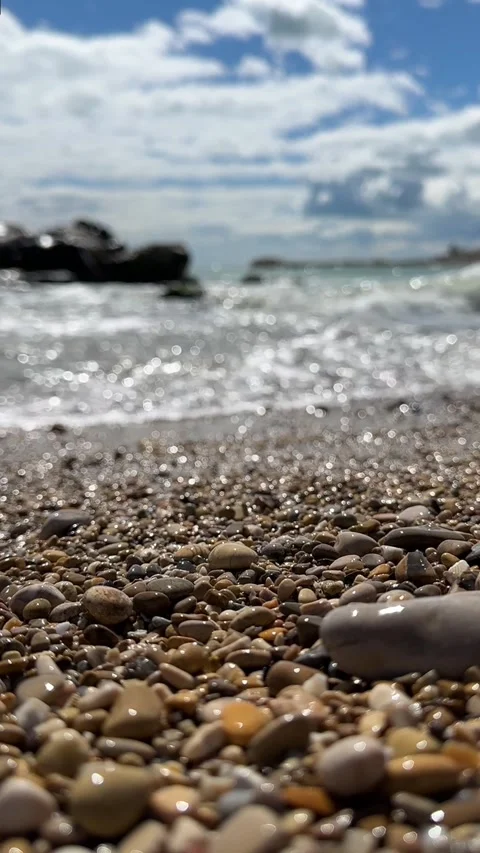 Pebbles in Focus with Blurred Seashore and Waves in Background Stock Footage 303352391