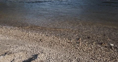 Pebbles on the river shore with waves lapping gently on the bank Stock Footage 127128709