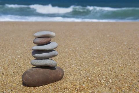 Pebbles stacked on a sandy beach in front of ocean and waves background Stock Photos