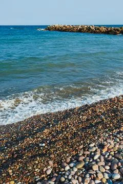 Pebbles of various sizes line the shore as gentle waves roll in, creating a p Stock Photos