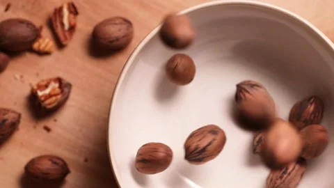 Pecan nuts in shell falling into bowl, slow motion. Video stock 171674488