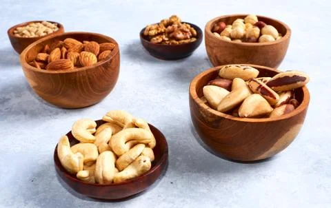 Pecans, hazelnuts, almonds, pine nuts, cashews in wooden bowls on blue backgr Photos