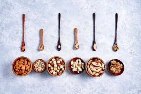 Pecans, hazelnuts, almonds, pine nuts, cashews in wooden bowls on blue backgr Stock Photos
