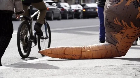 Pedastrians steps over tail of t rex costume mascot on city sidewalk Vidéo 84928998