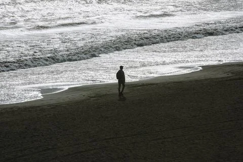 Pedestrian on the beach with sparkling reflection of sunlight on the sea surf Stock Photos