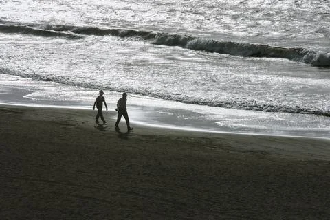Pedestrian on the beach with sparkling reflection of sunlight on the sea surf Stock Photos