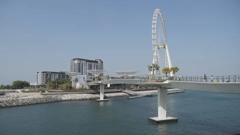 A pedestrian bridge with a massive ferris wheel on the waterfront. Stock Footage 308909731