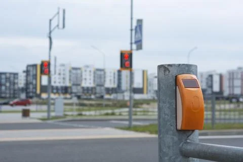 Pedestrian crossing button on metal post with blurred traffic lights and city Stock Photos