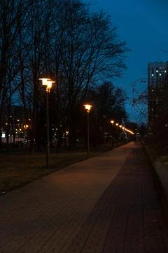 A pedestrian path illuminated by lanterns in the evening, in December Stock Photos