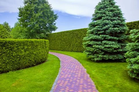 Pedestrian path made of red stone tiles is curved in an arc in the park. Stock Photos