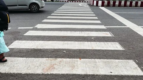 A pedestrian walks across a marked zebra crossing at a busy road intersection Stockbeeldmateriaal 340975112