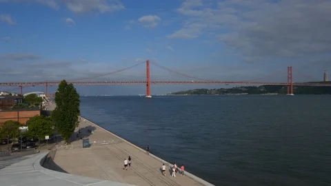 Pedestrian walkway riverside to Tagus River with view of 25 April Bridge in Stock Footage 130008167