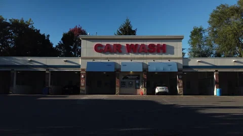 Pedestrian wipes frame, white car pulls into a car wash bay and parks, wide shot Stock-Footage 320890473