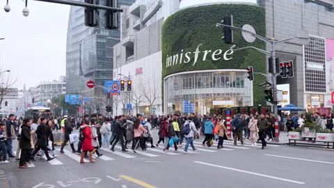 Pedestrians cross a busy intersection in front of a multi-story retail building Stock Footage 330976951