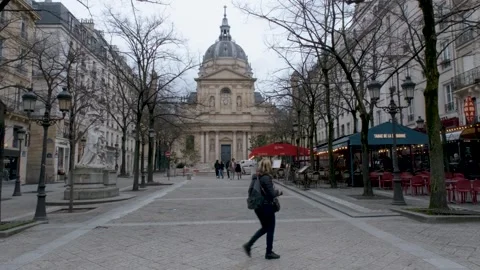 Pedestrians cross the Place de la Sorbonne with the historic chapel rising Stock Footage 325844341