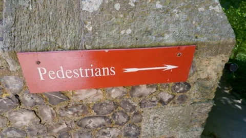 Pedestrians direction sign on stone wall, right pan revealing footpath and Vídeo Stock 342295526