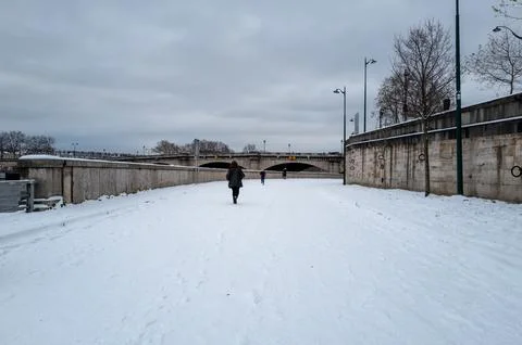 Pedestrians walking on a snow-covered quay along the Seine river in Paris Stock Photos