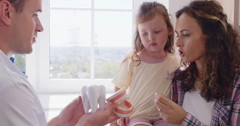 Pediatric dentist demonstrating brushing technique to mother and child at clinic Stock Footage 327607377