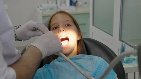Pediatric dentist examining teeth of a brave girl sitting in dental chair. Vidéo 340630366