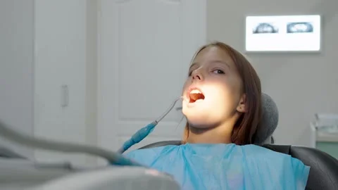 Pediatric dentist examining teeth of young girl sitting in dental chair. 库存影片 340630498