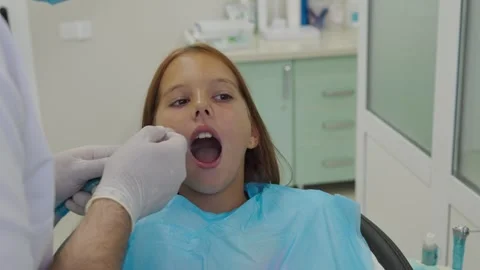 Pediatric dentist inserting saliva ejector for young girl during treatment. 库存影片 340630389