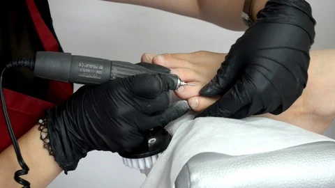 Pedicure master in red apron and gloves works with router with mill, on girl toe Stock Footage 123012498