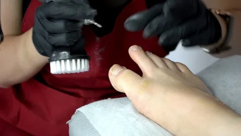 Pedicure master in red apron and gloves works with router with mill, on girl toe Stock Footage 123012724